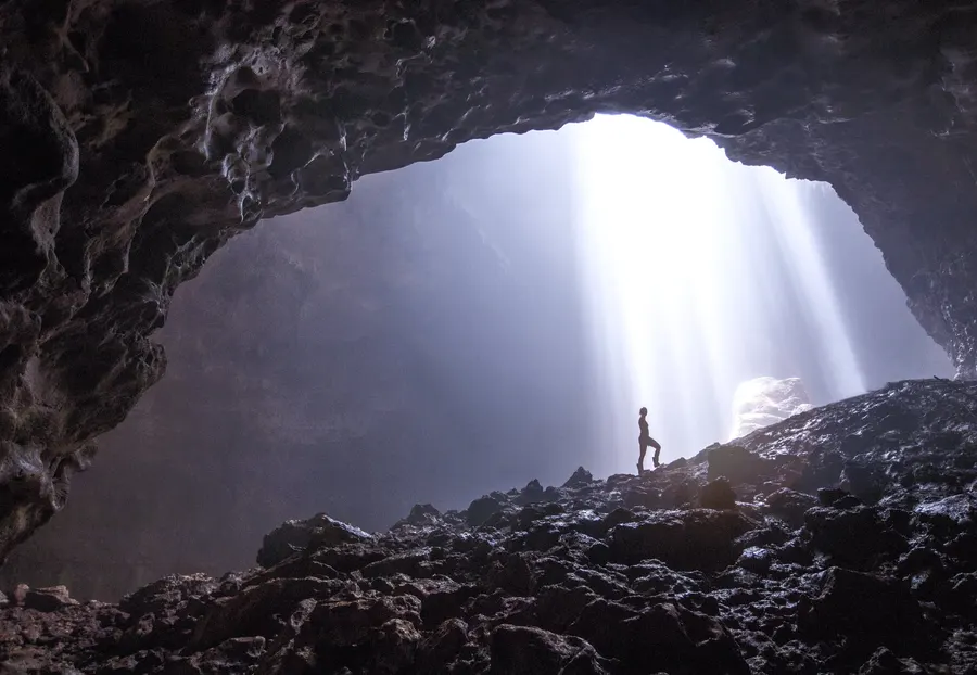 Shafts of light falling into Jomblang Cave, with a small figure standing below.