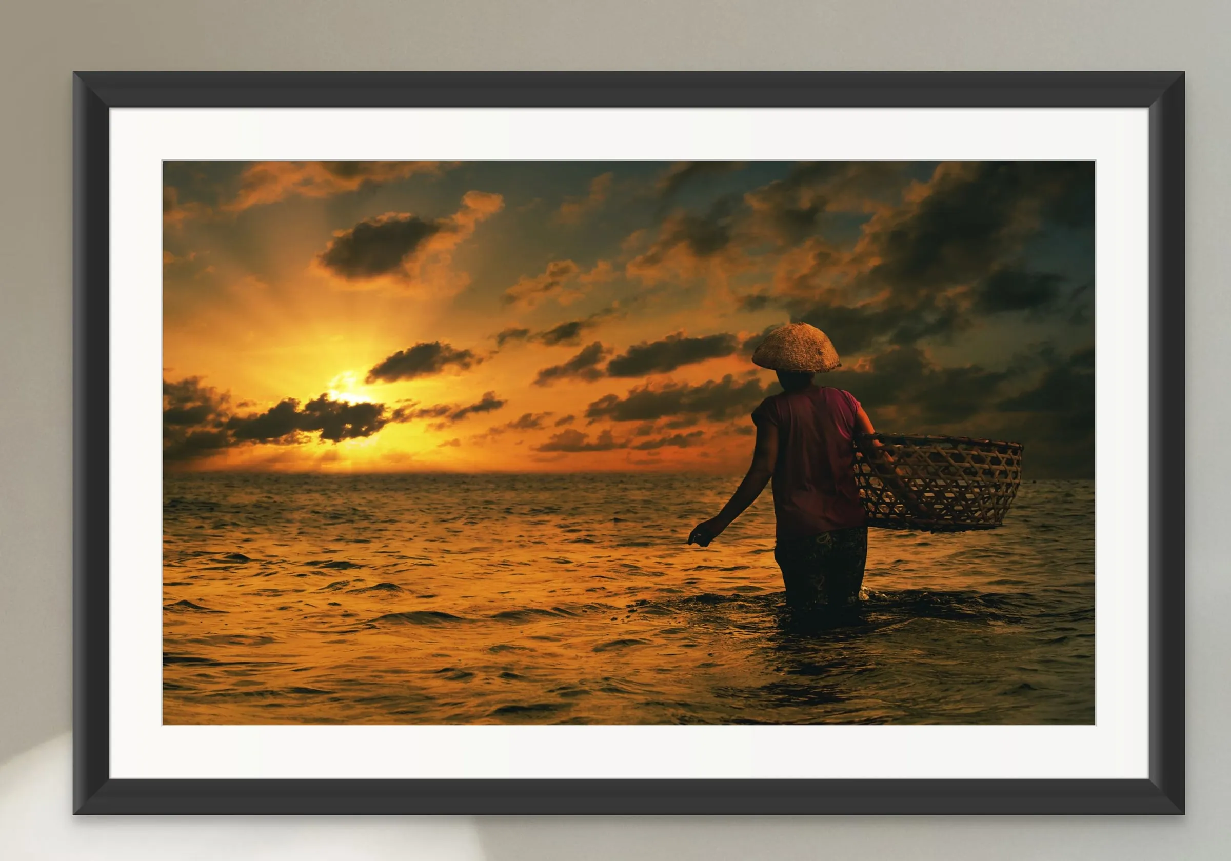Framed print of a fisher wading in the sea at sunset with a woven basket.