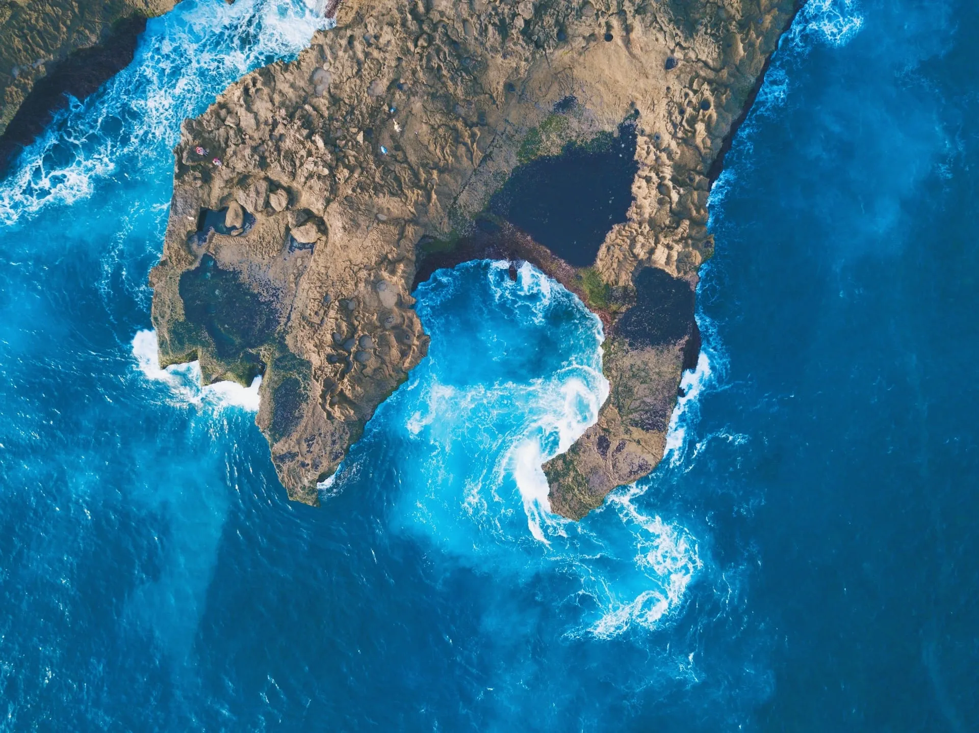 Aerial view of a rocky coastline with a natural arch and turquoise waves.