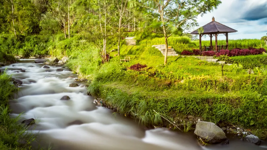 A tranquil stream with smooth, flowing water surrounded by lush greenery in Puncak, Indonesia.