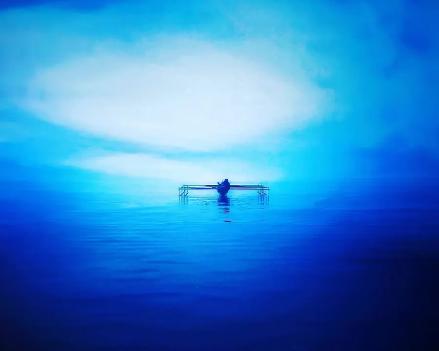 A small traditional boat carrying a solitary fisherman floats in expansive blue waters near West Papua.