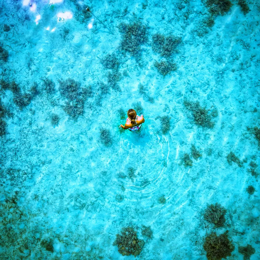 A person standing in the shallow, turquoise waters of Tiger Island in Indonesia’s Thousand Islands.
