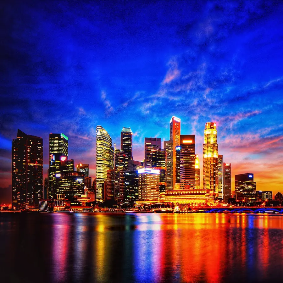 A city skyline at night with coloured lights reflected in the water.