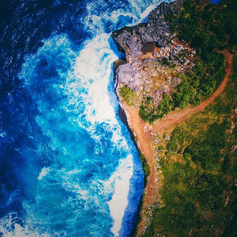 Waves breaking along a green headland, seen from above.