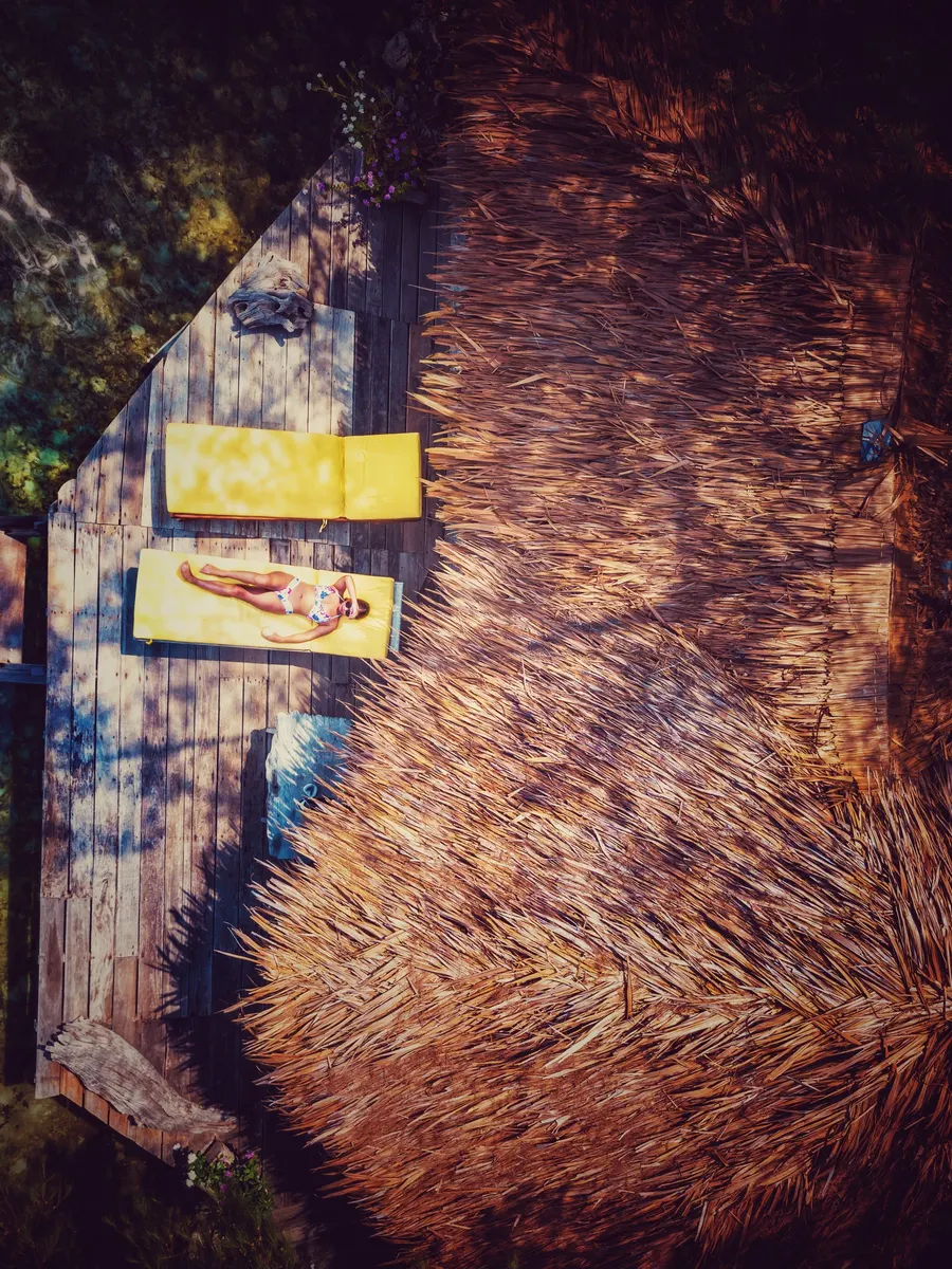 An aerial view of a wooden deck with yellow lounge chairs beside a large thatched roof on Tiger Island, Indonesia.